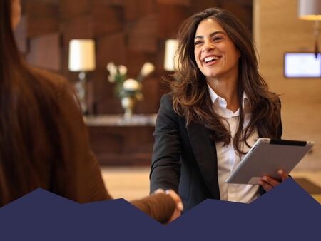 Hotel manager with a tablet welcoming a business guest with a handshake in a hotel lobby